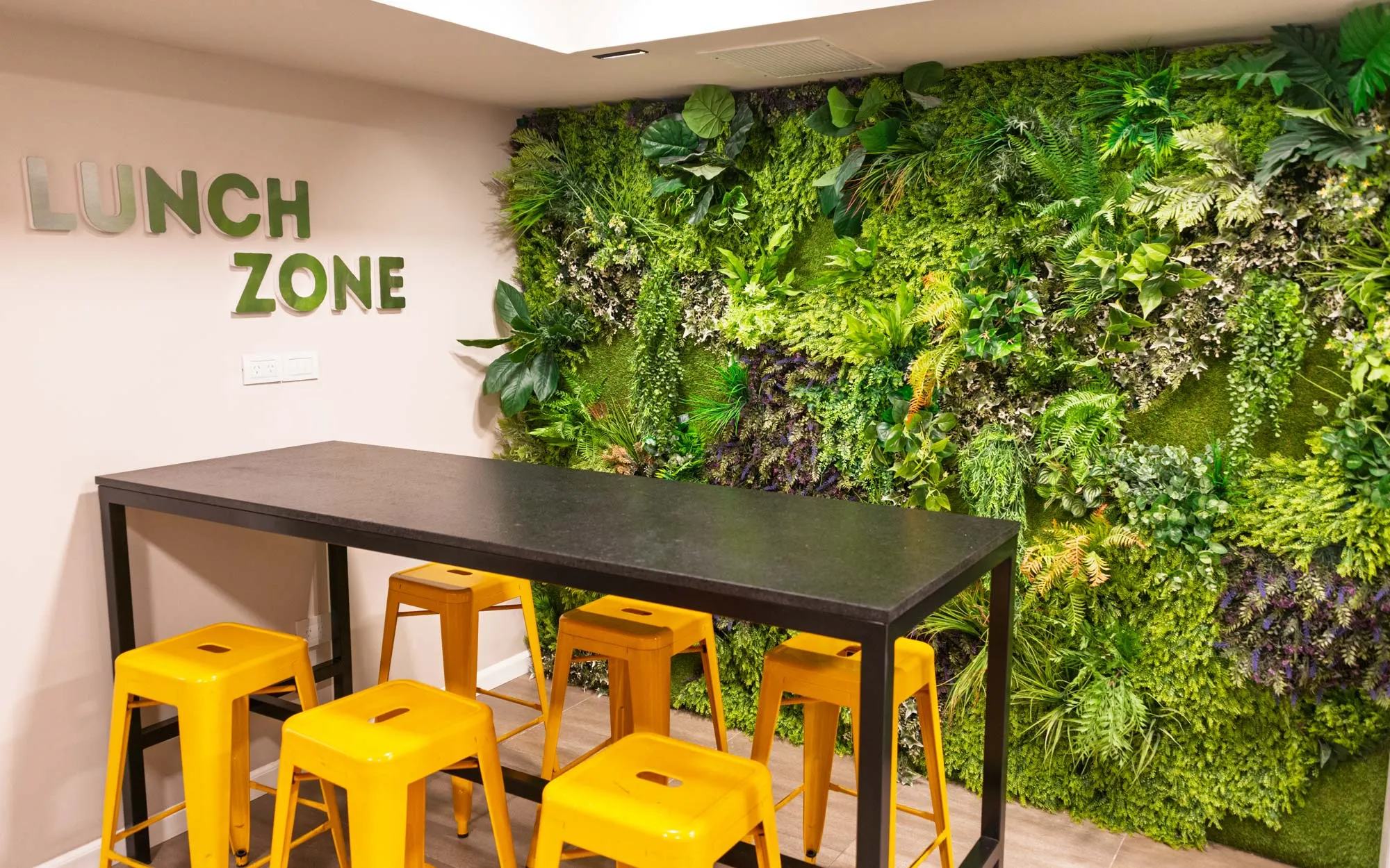 Espacio de almuerzo con jardín vertical y banquetas amarillas